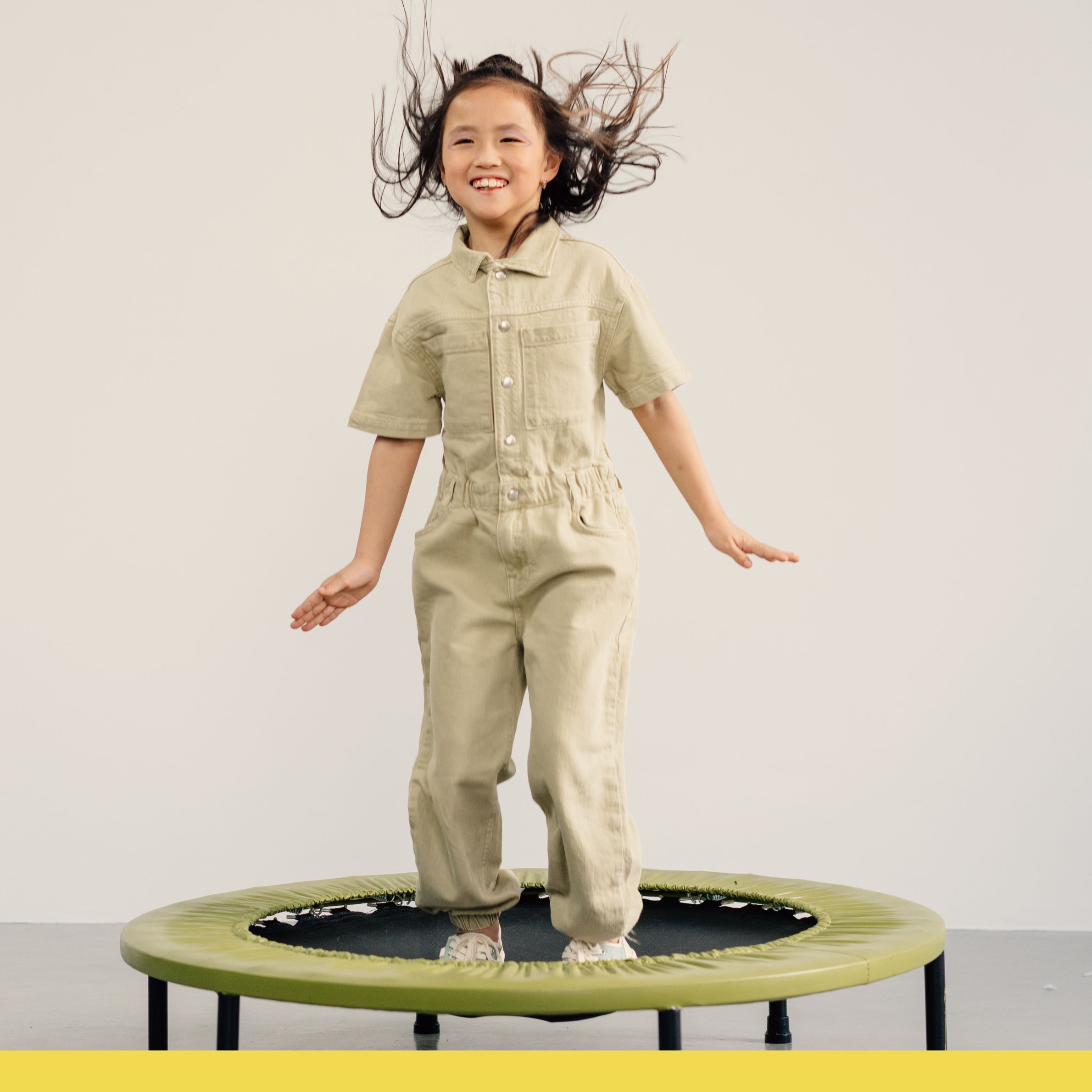 Young girl smiling while jumping on a green rebounder trampoline indoors